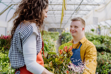 Experienced woman florist helping young employee with Down syndrome in garden centre.