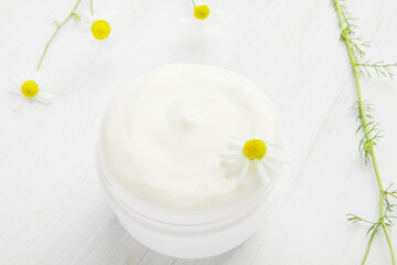 White nourishing cream with chamomile in a white jar.