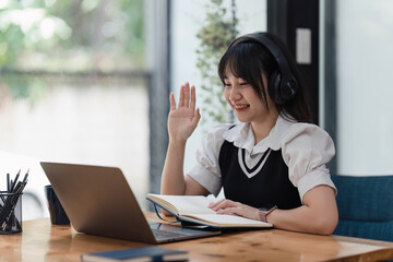 Online education, e-learning. Asian woman in stylish casual clothes, studying using a laptop, listening to online lecture, taking notes, online study at home