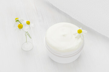 White nourishing cream with chamomile in a white jar.