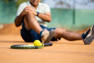 Close up shot focus on ball, senior middle aged tennis player got due to loss of tennis match or game during competition - concept of emergency, painful and inflammation
