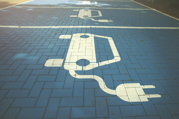 white electric car symbol painted on blue pavement. parking lot with charging station marked for...