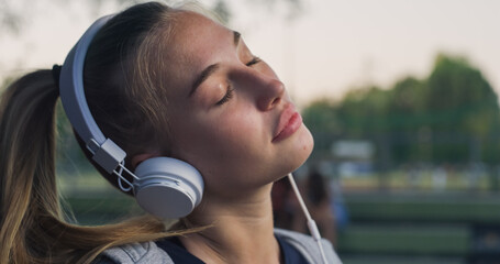 Closeup Portrait of Beautiful White Woman Smiling While Putting on her Headphones in the Park During her Early Morning Walk. Female Teenager Enjoying Music and Fresh Air While Being Outdoors 