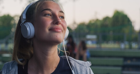 Closeup Portrait of Beautiful White Woman Smiling While Putting on her Headphones in the Park During her Early Morning Walk. Female Teenager Enjoying Music and Fresh Air While Being Outdoors 