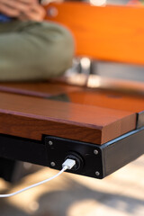 Close up outdoor image of smartphone charging via USB  with help of solar panel installed inside wooden bench. Modern technologies, alternative sources of energy. Environment concept. 