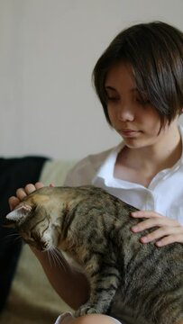 A teenage girl stroking her cat at home. Love and affection for pets. 25 fps vertical 4k footage.