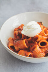 Vegetarian pasta with tomato sauce and curd cheese in white bowl, gray background.