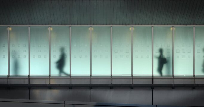 The silhouettes of people walking behind frosted glass in a train station in Tokyo. This video loops seamlessly.