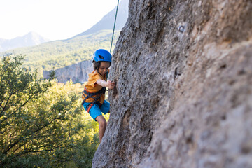Children's rock climbing. The boy climbs a rock against the backdrop of mountains. Extreme hobby....