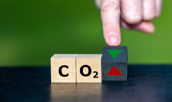 Symbol for reducing CO2 emissions. Hand turns a wooden cube and changes the orientation of an arrow from up to down.
