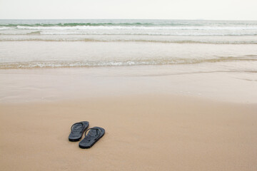 Fototapeta na wymiar Black slippers feet at the beach, with a wave of foaming gentle beneath them.