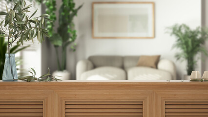 Wooden table top, cabinet, panel or shelf with shutters close up. Olive branch in vase and candles. Blurred background, white living room with fabric sofa, interior design