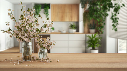 Wooden table, desk or shelf close up with branches of cherry blossoms in glass vase over blurred...