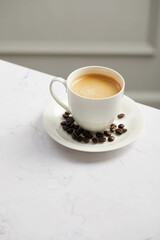 Cup of coffee and beans, on white marble table