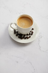 Cup of coffee and beans, on white marble table