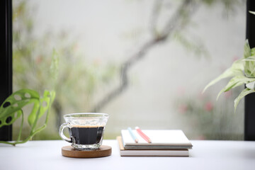 Naklejka na ściany i meble Coffee with crema in a a glass cup and notebooks on wooden table with plants