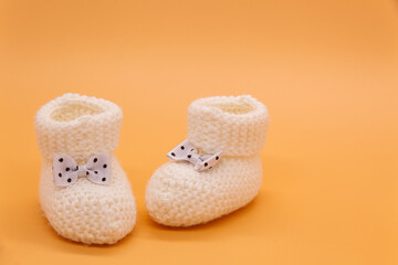 White knitted baby booties with bows on orange isolated background