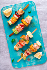 Grilled trout skewers with corn, zucchini and pepper served on turquoise board. Hot fish meal. Top view