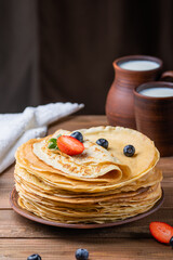 Pancakes with strawberries and blueberries, jug of milk, ceramic dishes in rustic style
