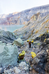 Miners carrying baskets of sulphur out of Ijen crater. Workers extract sulfur and carry a 80-90 kg. basket full of sulfur on their shoulder at Kawah Ijen volcano in East Java,  Indonesia.
