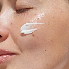 Cream smear. Beuaty close up portrait of young woman with a healthy skin is applying a facial skincare product. Face  daily care routine - obrazy, fototapety, plakaty