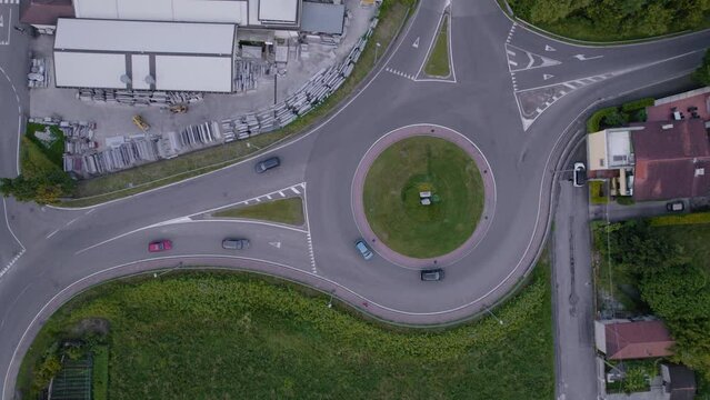 Top view of a roundabout on a road with little traffic and lots of nature on the sides. Camera points down and moves from left to right, dolly