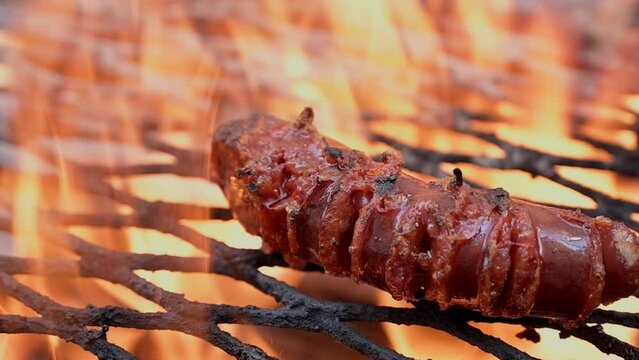 A close-up of a sausage grilling over an open fire, with flames licking the sides and creating a delicious char.