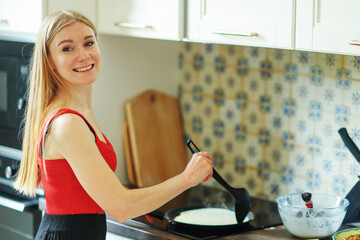 Woman prepares pancakes in a bright kitchen. Chef at home