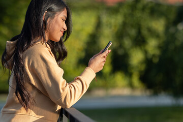 Happy woman walking and writing or reading sms messages online on a smartphone while the wind moves her hair on a street