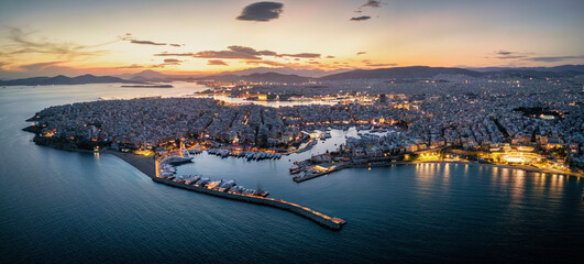 Fototapeta premium Aerial view of the illuminated Piraeus district in Athens, Greece, with Zea Marina, Kastella hill and the ferry boat harbour in the background during dusk