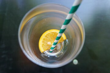 Leeres Glas mit Eiswürfel, Zitronenscheibe und grün-weißem Strohhalm auf grüner Tischplatte 