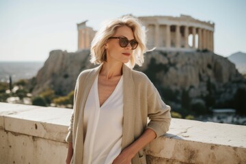 Fototapeta na wymiar Fashionable blonde woman in sunglasses and coat posing at the top of the Acropolis in Athens, Greece