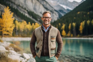 Handsome middle age man in sweater and eyeglasses standing in front of mountain lake.