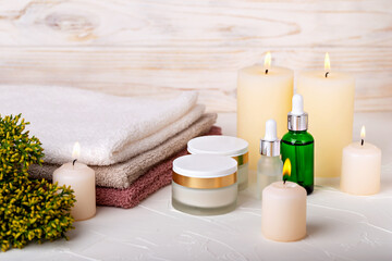 Obraz na płótnie Canvas Cosmetics, burning candles, towels and juniper branch on light background. Cream or lotion, oil or gel, skin care, spa treatments. The concept of peace, comfort. Selective focus