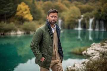 Handsome man in a green jacket standing in front of a waterfall