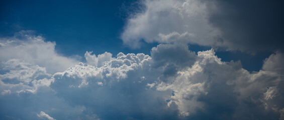Panoramic view of dramatic summer cumulus clouds in a bright blue sky.
