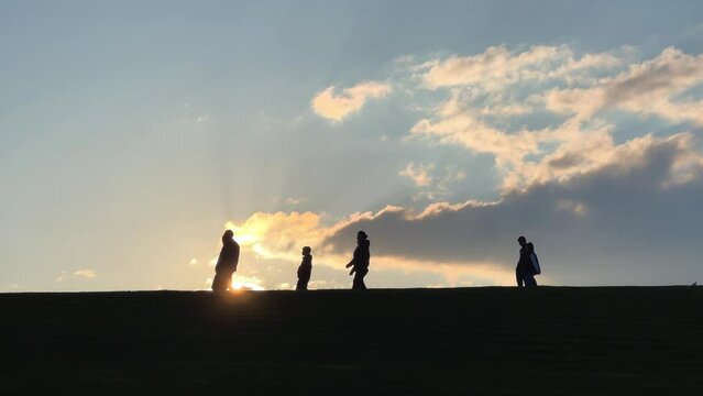 People walk against the background of sunlight near the monument to the Motherland. Spring light. People are walking on the hill. The setting sun. VOLGOGRAD, RUSSIA - MAY 2023