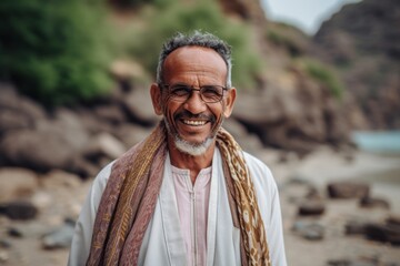 Portrait of a happy indian senior man with traditional clothing and glasses at the beach.