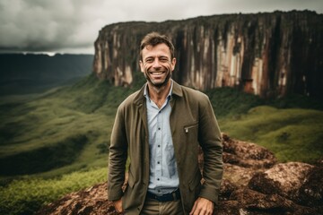 Handsome man in casual clothes is standing on the edge of the cliff and smiling at camera.