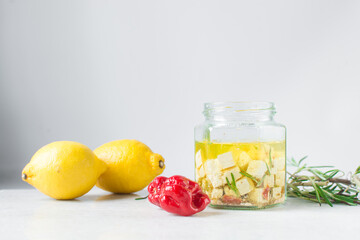Marinated feta cheese cubes in olive oil in a glass jar. Cheese cubes marinating in olive oil, feta cheese in olive oil with rosemary with dried pepper and tomatoes