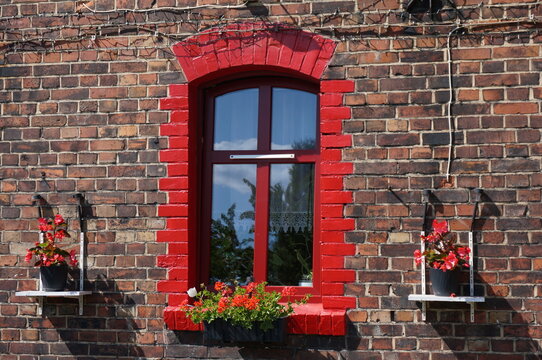 Red window with red flowers of old brick tenement house. Ruda Slaska, Poland.