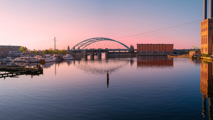 Fototapeta na wymiar Sunset over the tranquil Providence River with arching highway bridge, moored boats, and water reflections in Rhode Island