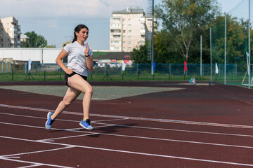 Obraz premium Young girl running on the running track at the stadium outdoors