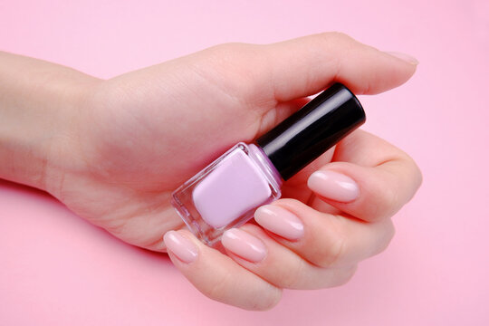 The hands of a young girl hold a bottle of pink gel nail polish on a pink background.The concept of hand and nail care, manicure, beauty salon, nail extension
