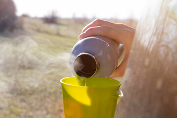 Girl tourist drinks hot tea from a thermos. Mug of hot tea in nature. Travel and tourism concept.