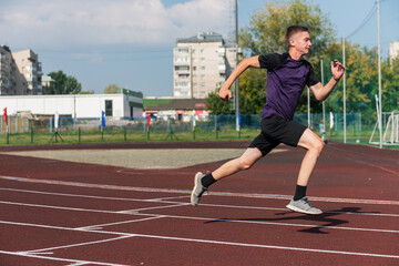 Obraz premium Young teen boy running on the running track at the stadium outdoors