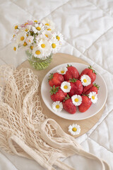 A plate of strawberries is decorated with white daisies. Berries with vitamins