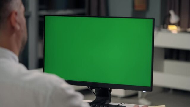 Man Working At Computer With Green Mock Up Screen in Home. Close Up Desktop Computer Monitor with Mock Up Green Screen Chroma Key Display
