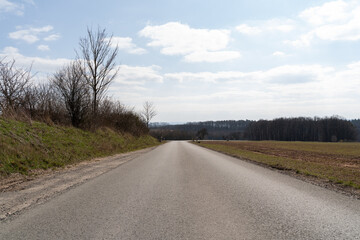 Asphalt road in the landscape with leafless trees and a bright sky on a sunny day in spring