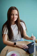 Beautiful young woman drawing a sketch with a stylus pen on a tablet computer in a cafe. Freelance...